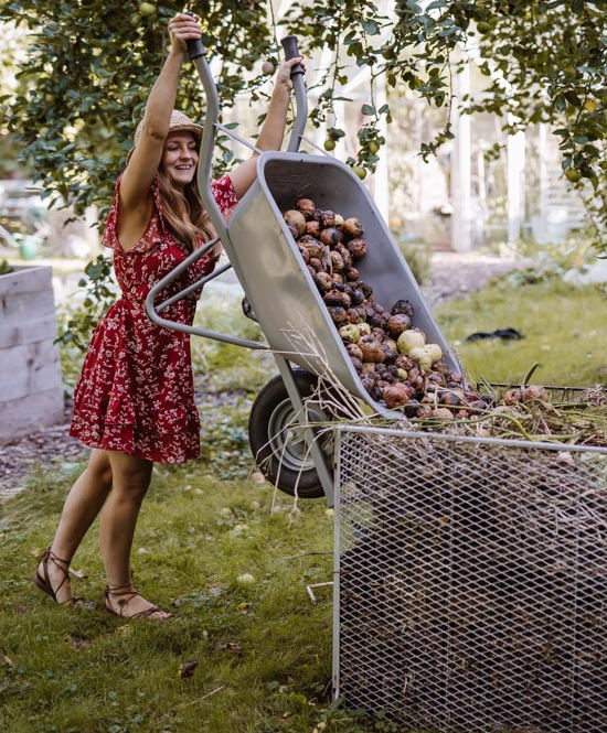 Frau schüttet mit Schubkarree Essensreste in Kompost.