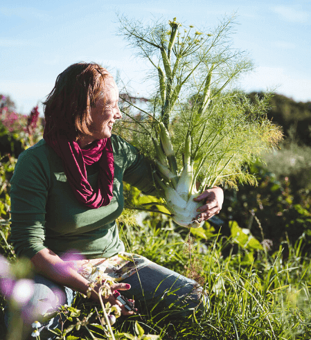 Frau mit Pflanze in der Hand im Permakultur-Garten