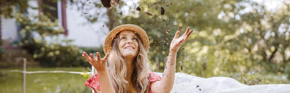 Frau wirft Mulch in die Luft im Selbstversorger*innen-Garten